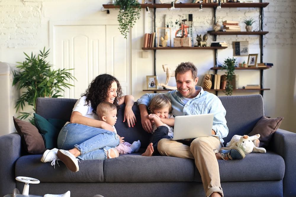 Two parents on a couch with their young children, looking at a laptop together
