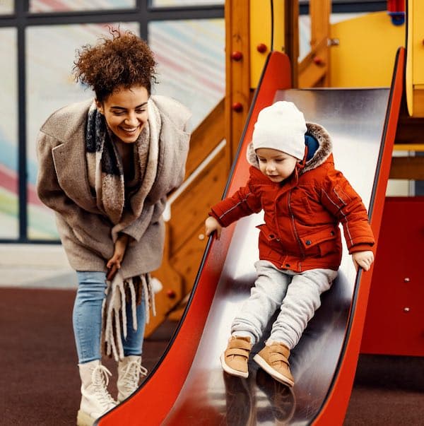 A mother pushing her young daughter on a playground swing on a bright afternoon