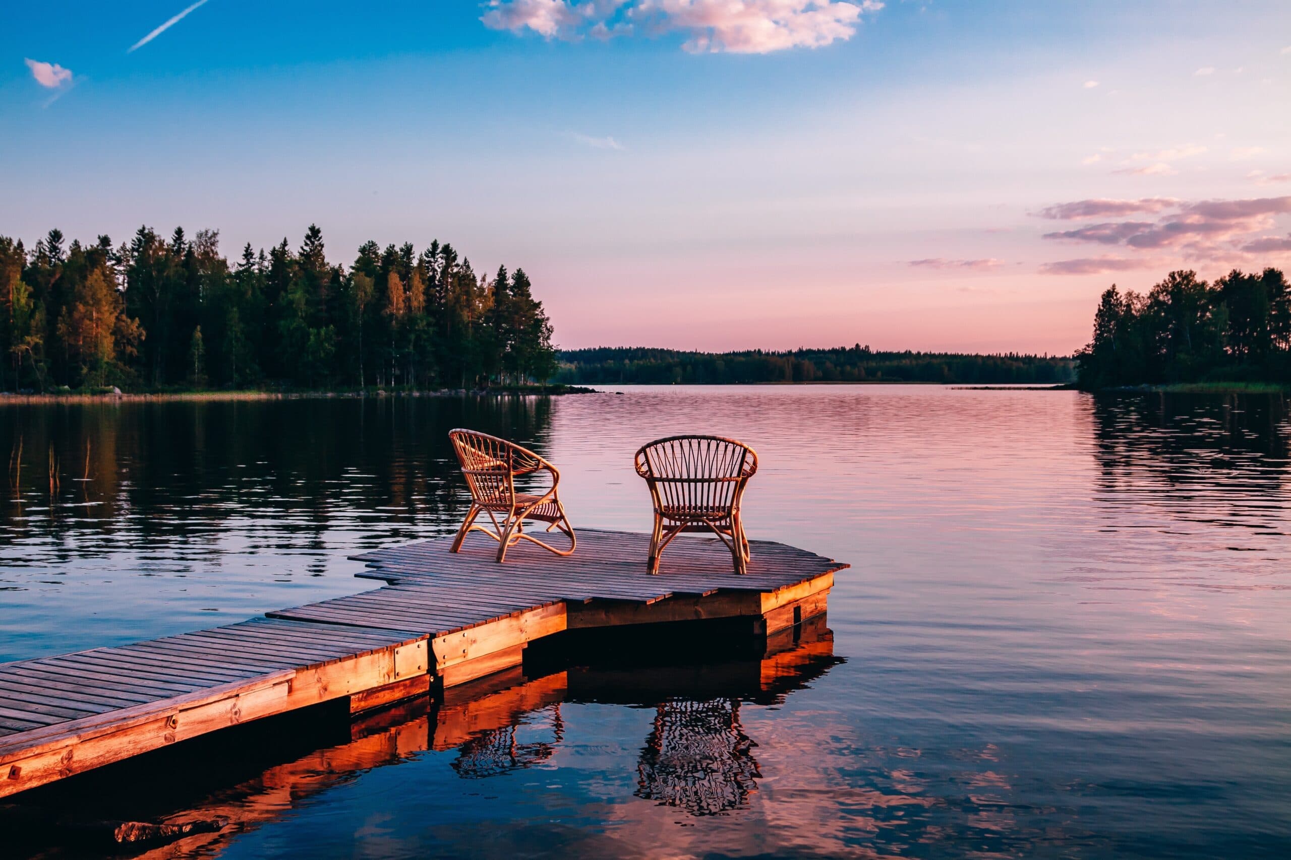Two empty wooden chairs at the end of a dock on still water in the late afternoon