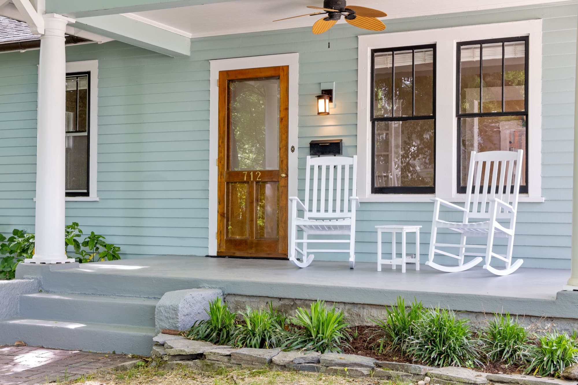 Two white rocking chairs beside a wooden screen door on a clapboard porch