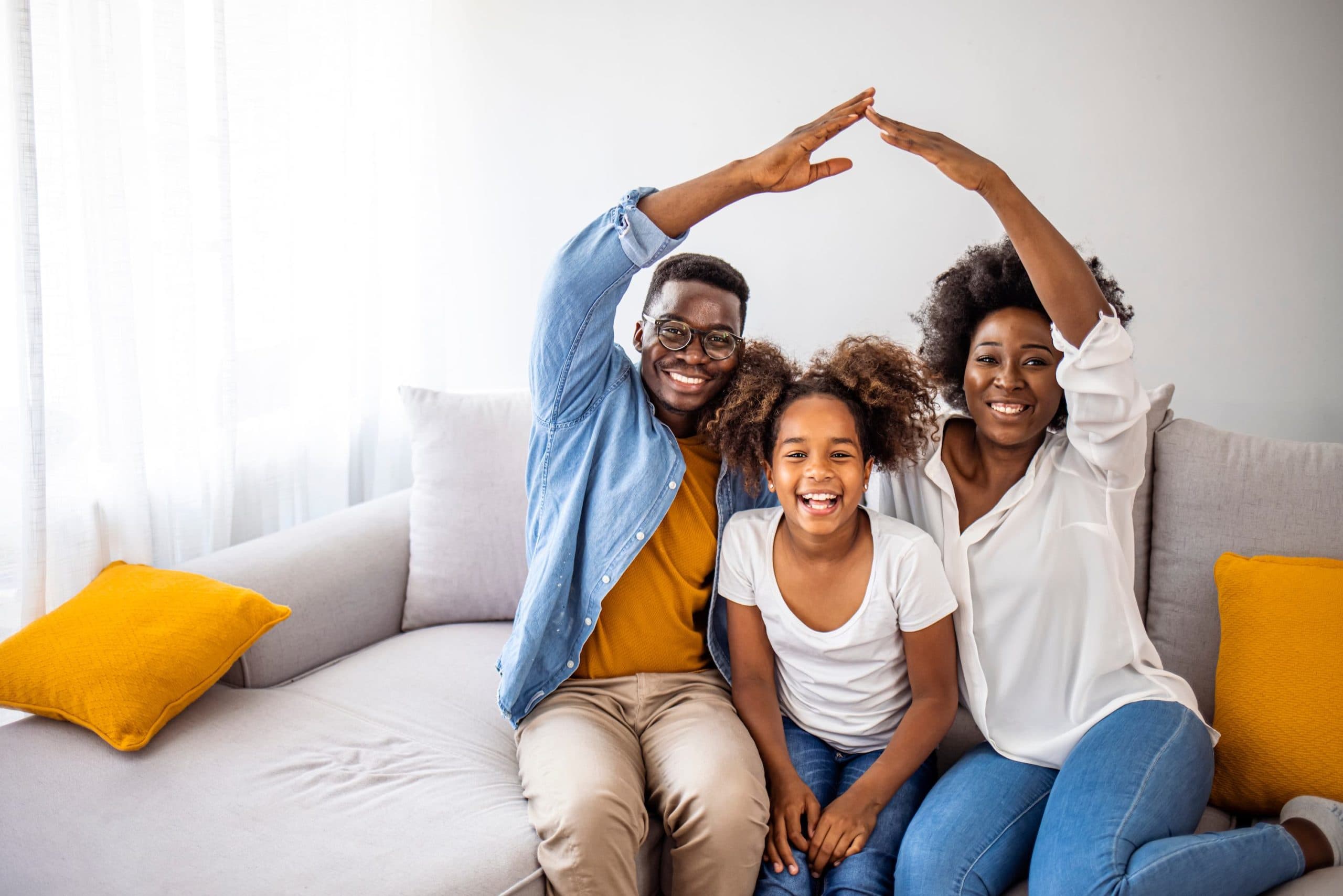 Parents on a couch with their daughter, arms raised to form the shape of a roof above her